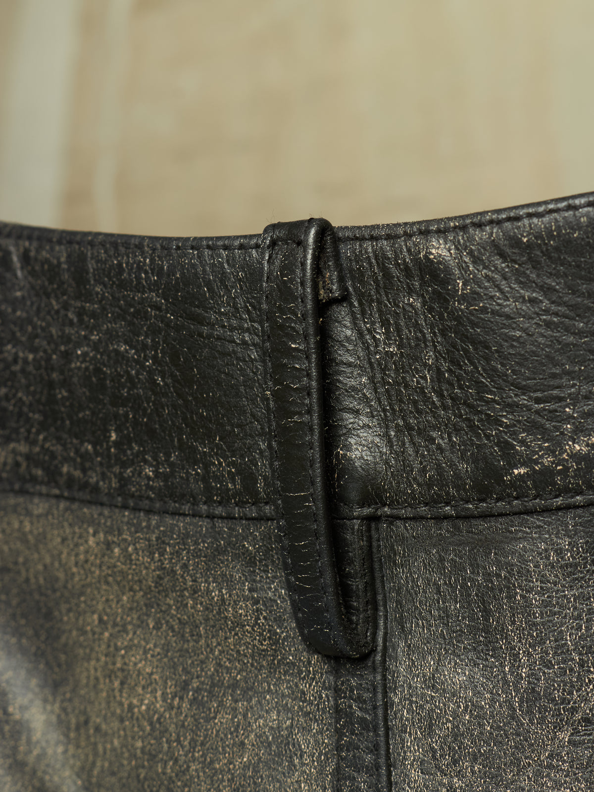 Close-up of a black distressed leather belt with a textured, weathered finish and a matching leather keeper loop.