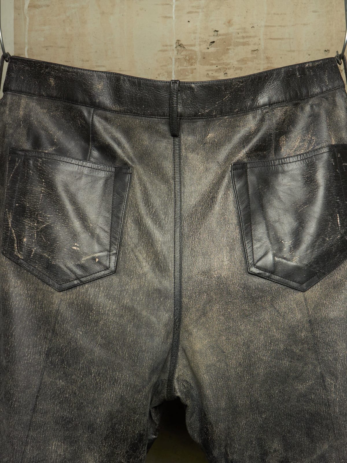 Distressed black leather shorts with a distressed finish, featuring two back patch pockets and a central seam, shown hanging against a neutral background.
