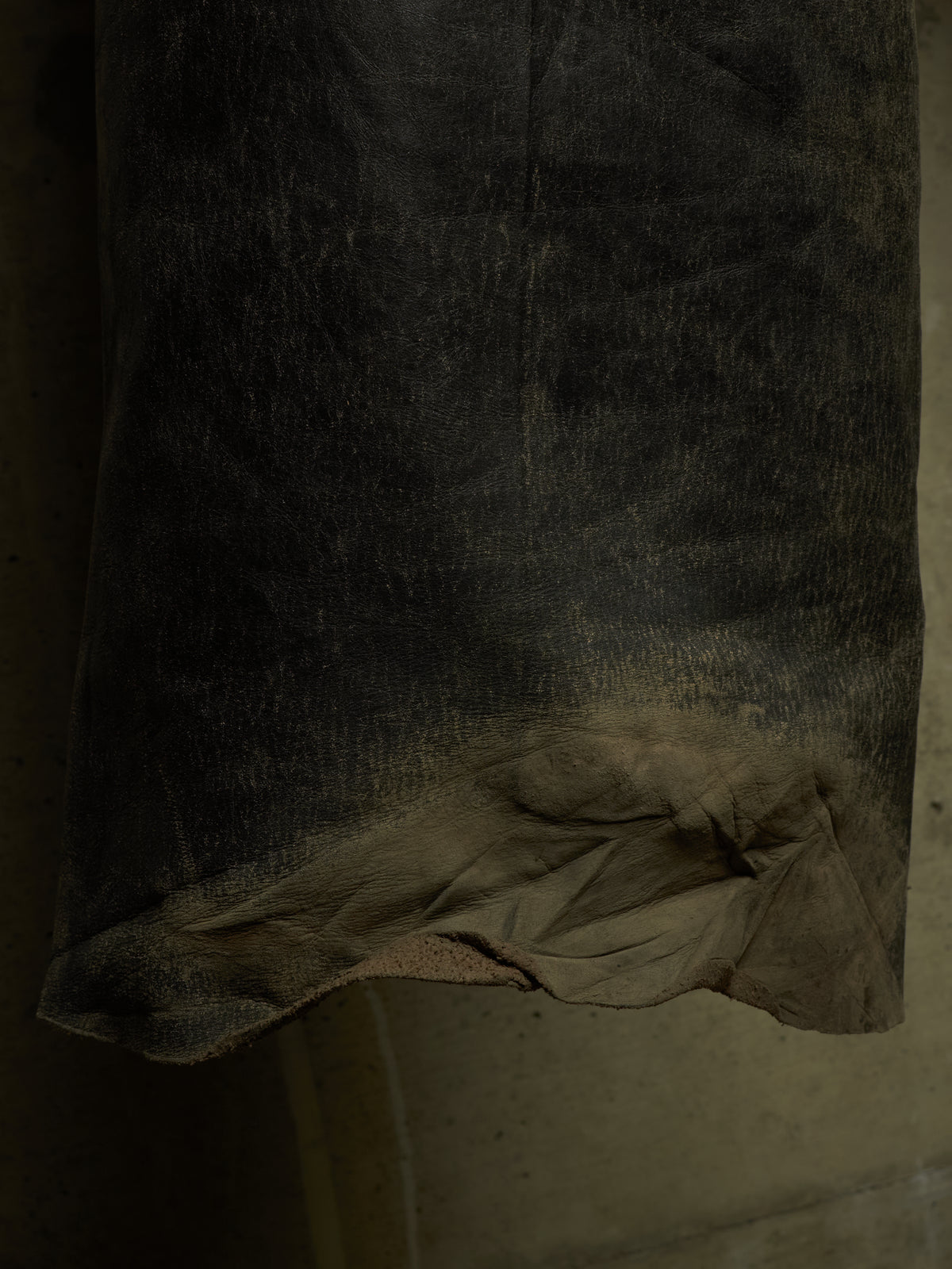 A close-up of a dark, heavily distressed leather or suede material with a frayed, worn edge showing a lighter tan underside.
