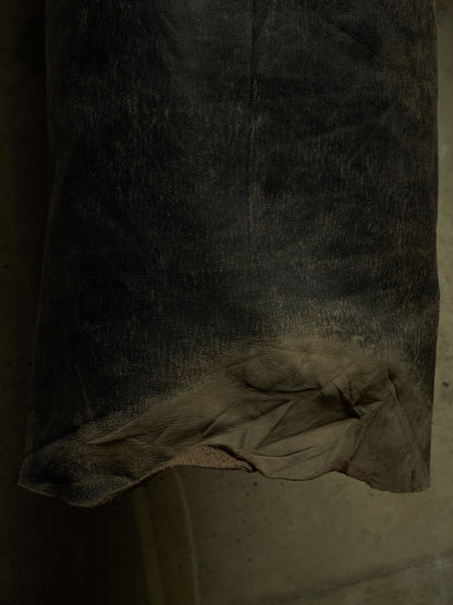 A close-up of a dark, heavily distressed leather or suede material with a frayed, worn edge showing a lighter tan underside.