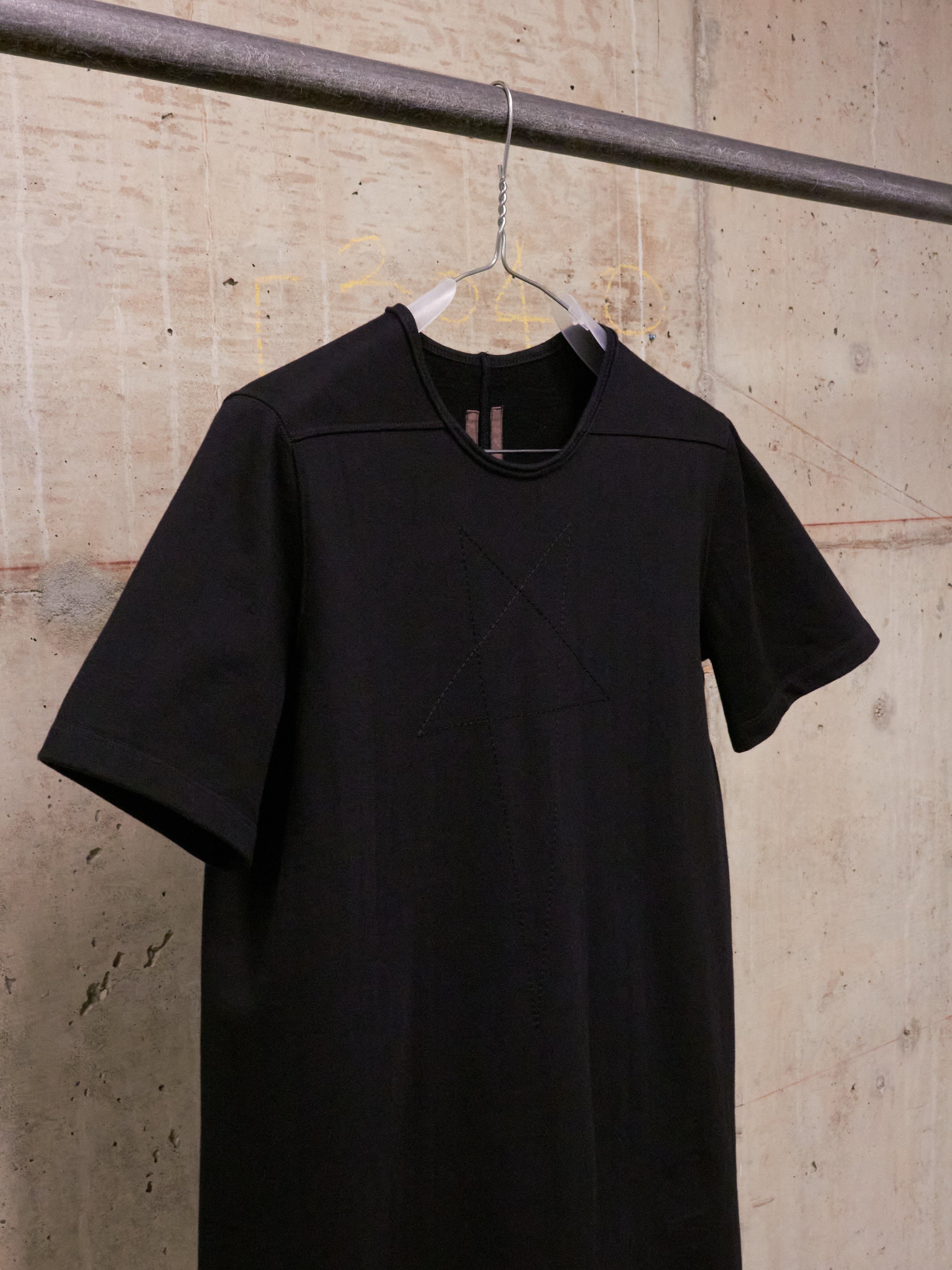 Black t-shirt on a hanger against a textured wall.