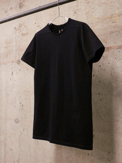 Black t-shirt hanging on a hanger against a textured wall.