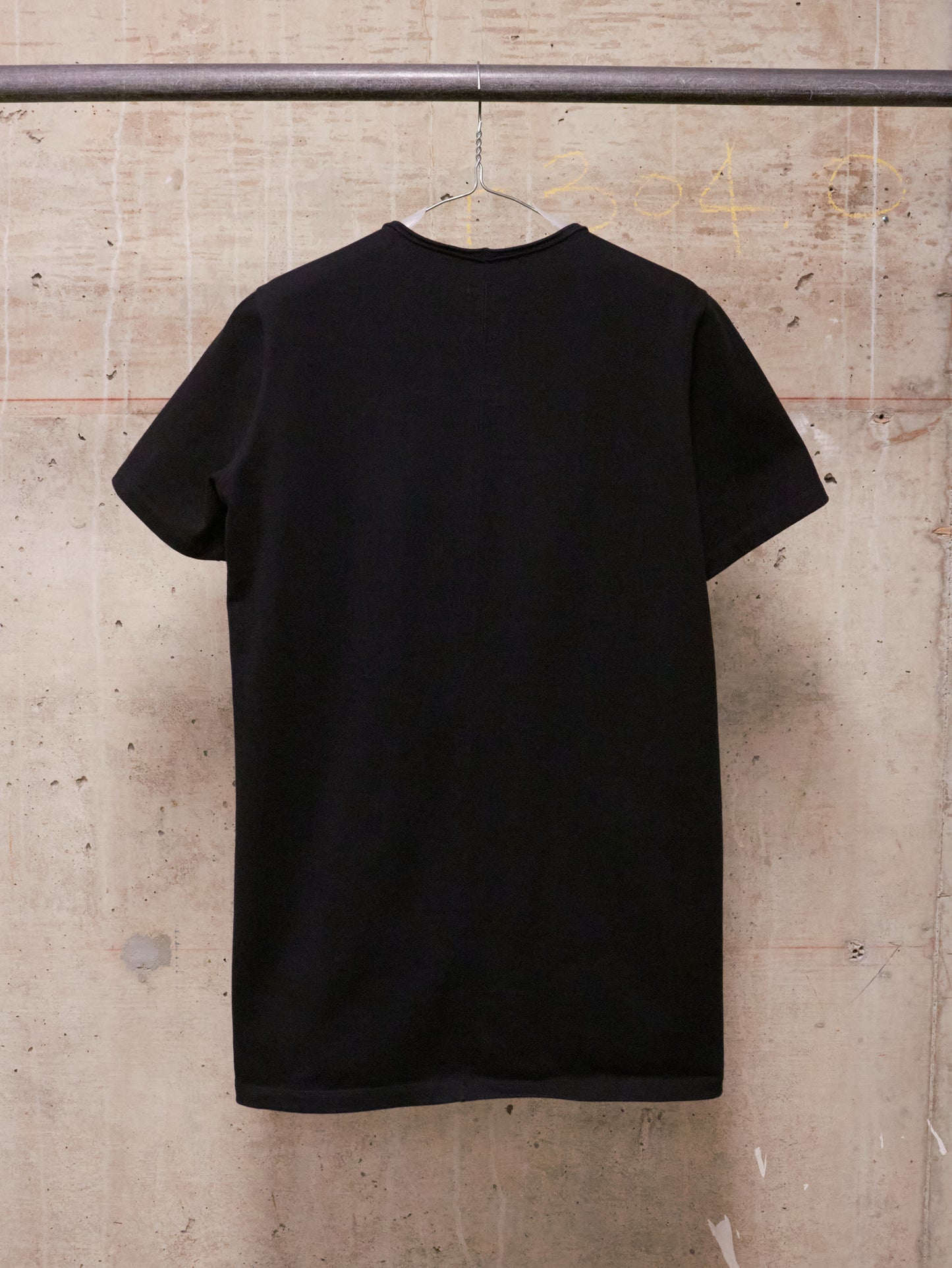 Black t-shirt on a hanger against a textured wall.