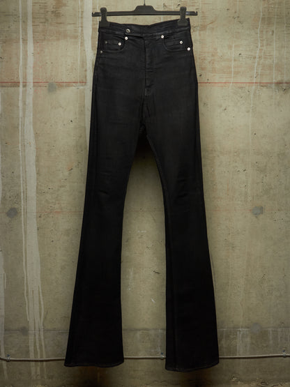 Black flare jeans hanging on a black hanger against a textured concrete wall.
