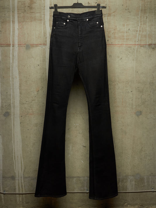 Black flare jeans hanging on a black hanger against a textured concrete wall.