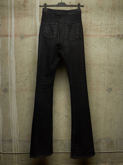 Black flare jeans hanging from a black hanger against a textured concrete wall.