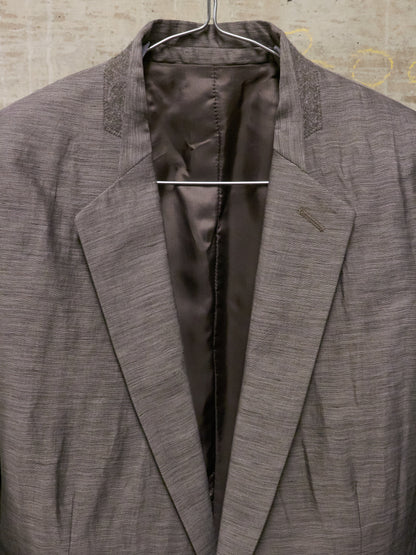 Gray blazer on a hanger against a textured wall.