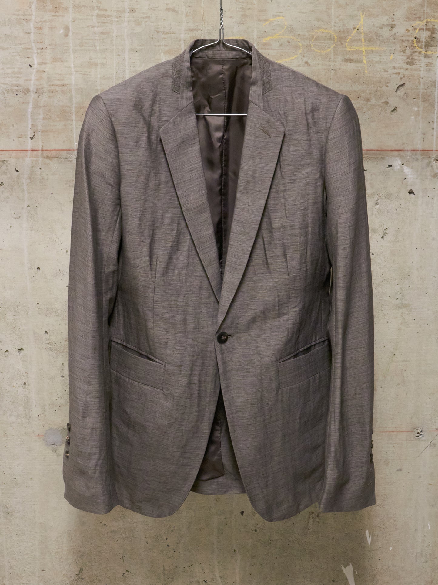 Brown blazer on a hanger against a textured wall.