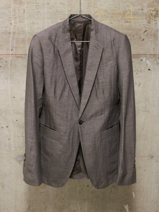 Brown blazer on a hanger against a textured wall.
