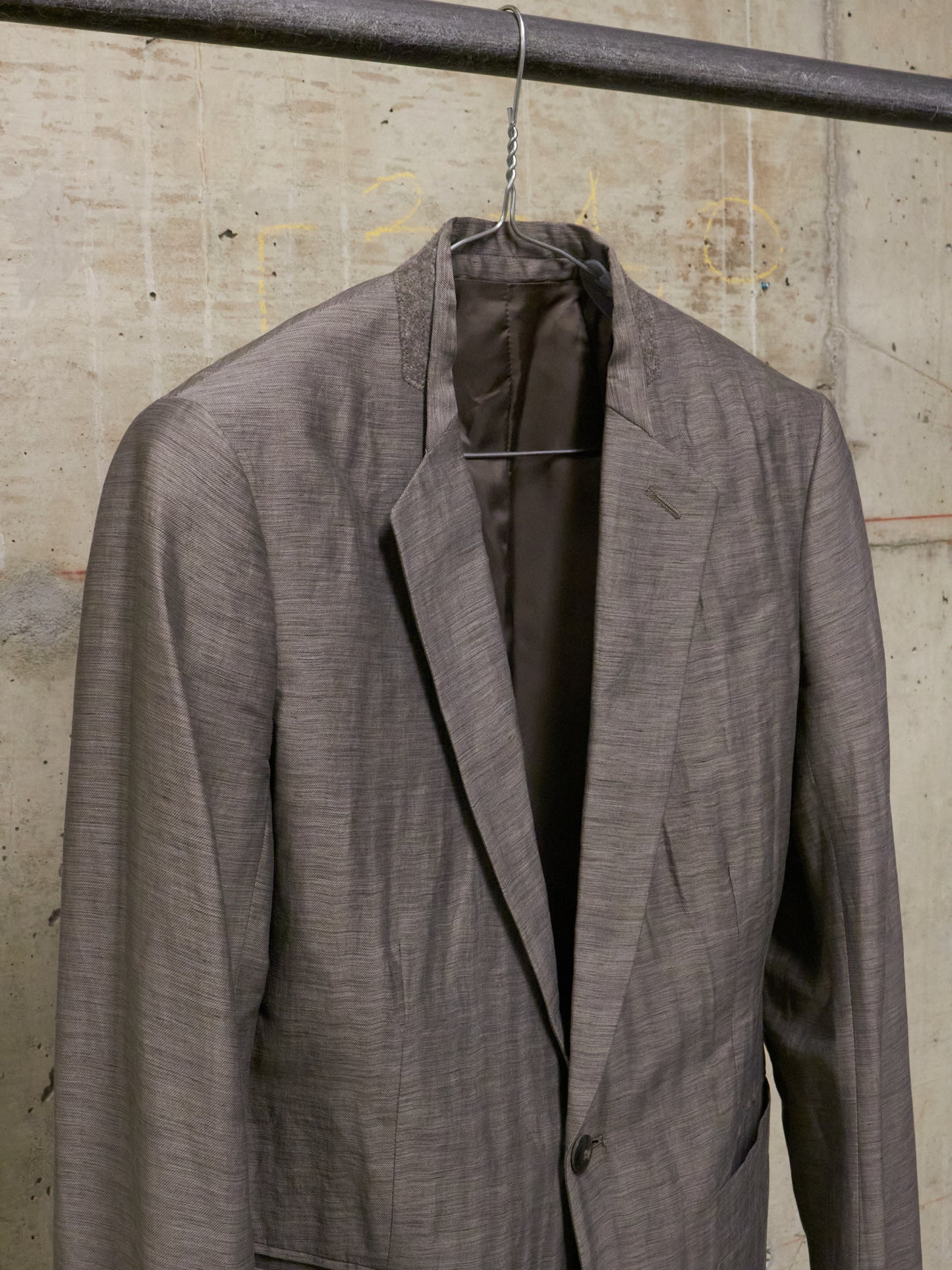 Gray suit jacket on a hanger against a concrete wall.