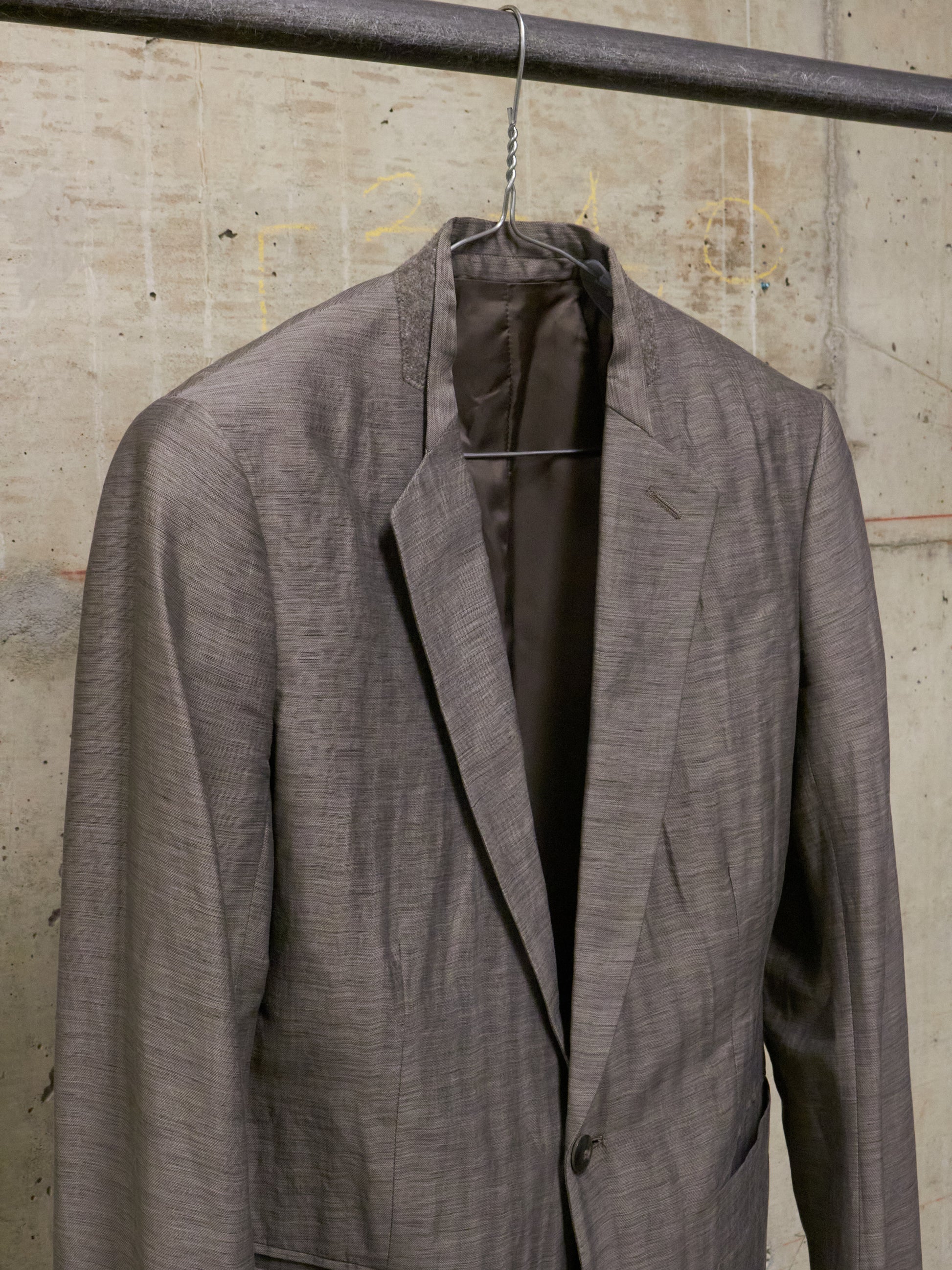 Gray suit jacket on a hanger against a concrete wall.