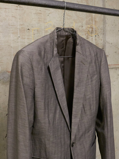 Gray suit jacket on a hanger against a concrete wall.
