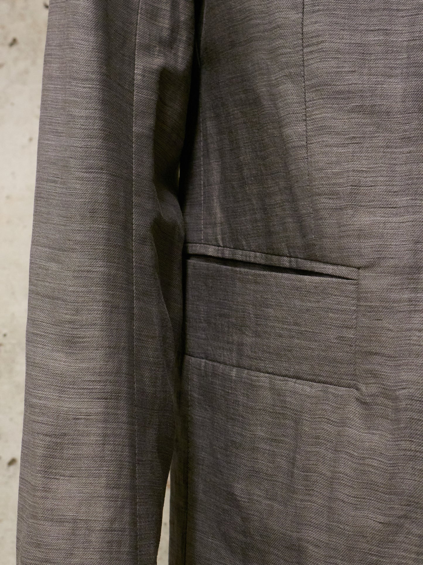 Close-up of a gray textured fabric with a pocket detail on a neutral background