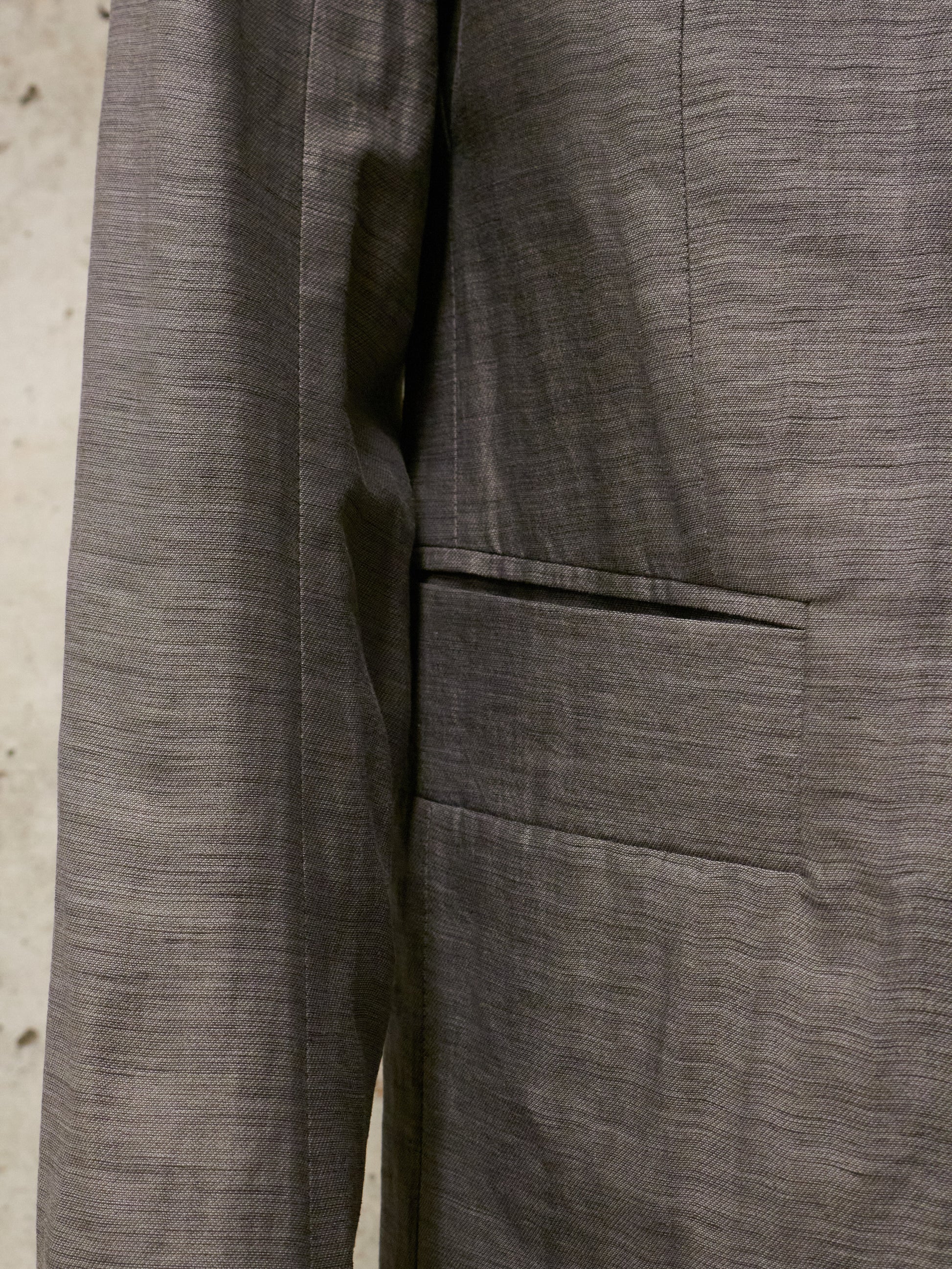 Close-up of a gray textured fabric with a pocket detail on a neutral background
