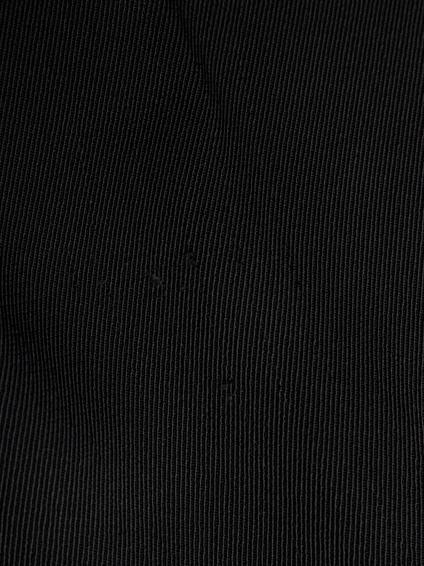 A close-up of black fabric with a fine vertical ribbed texture.