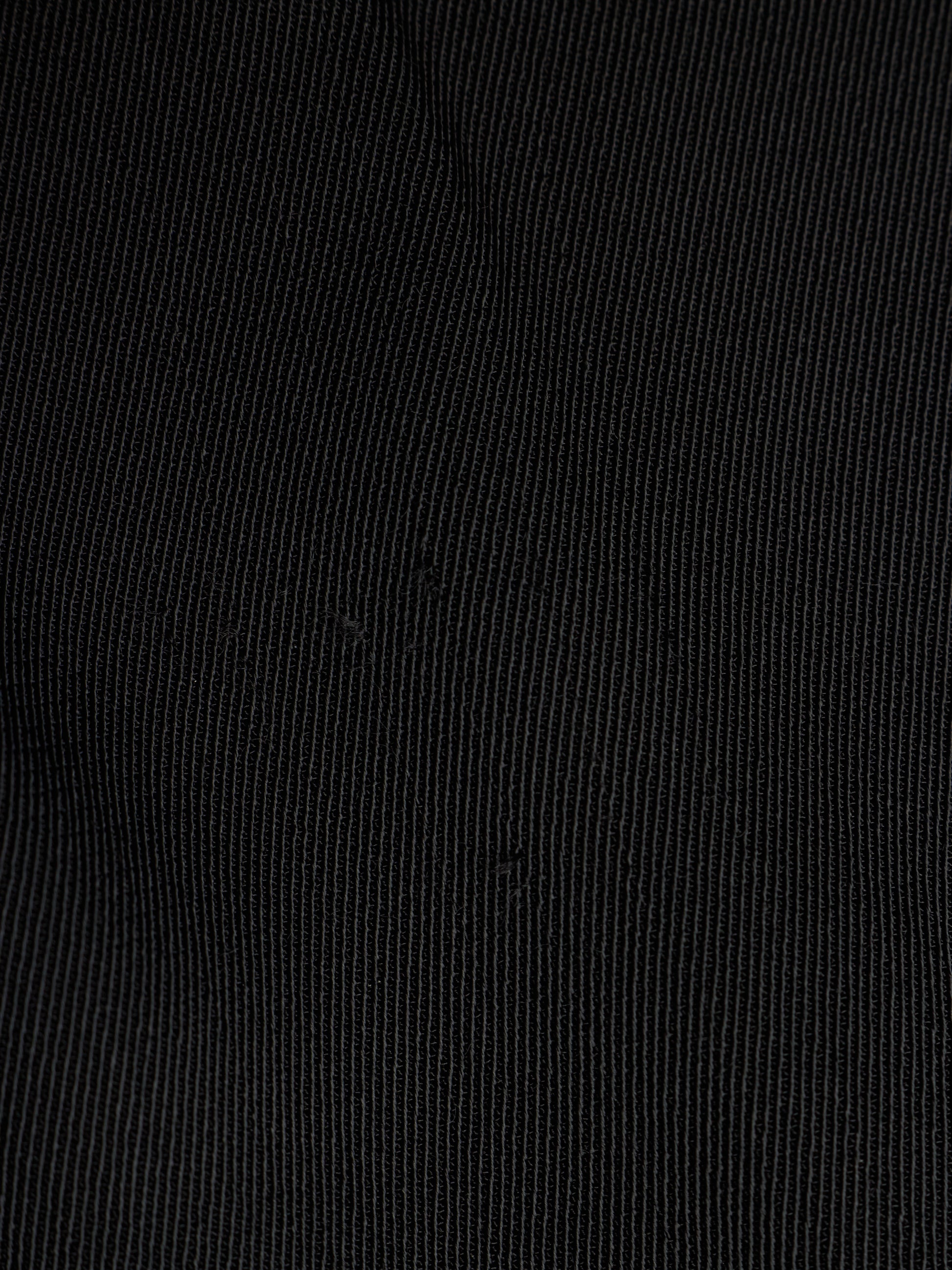 A close-up of black fabric with a fine vertical ribbed texture.