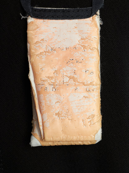 A close-up of a rectangular beige fabric pouch or pocket with a black strap at the top, shown against a black textured background.