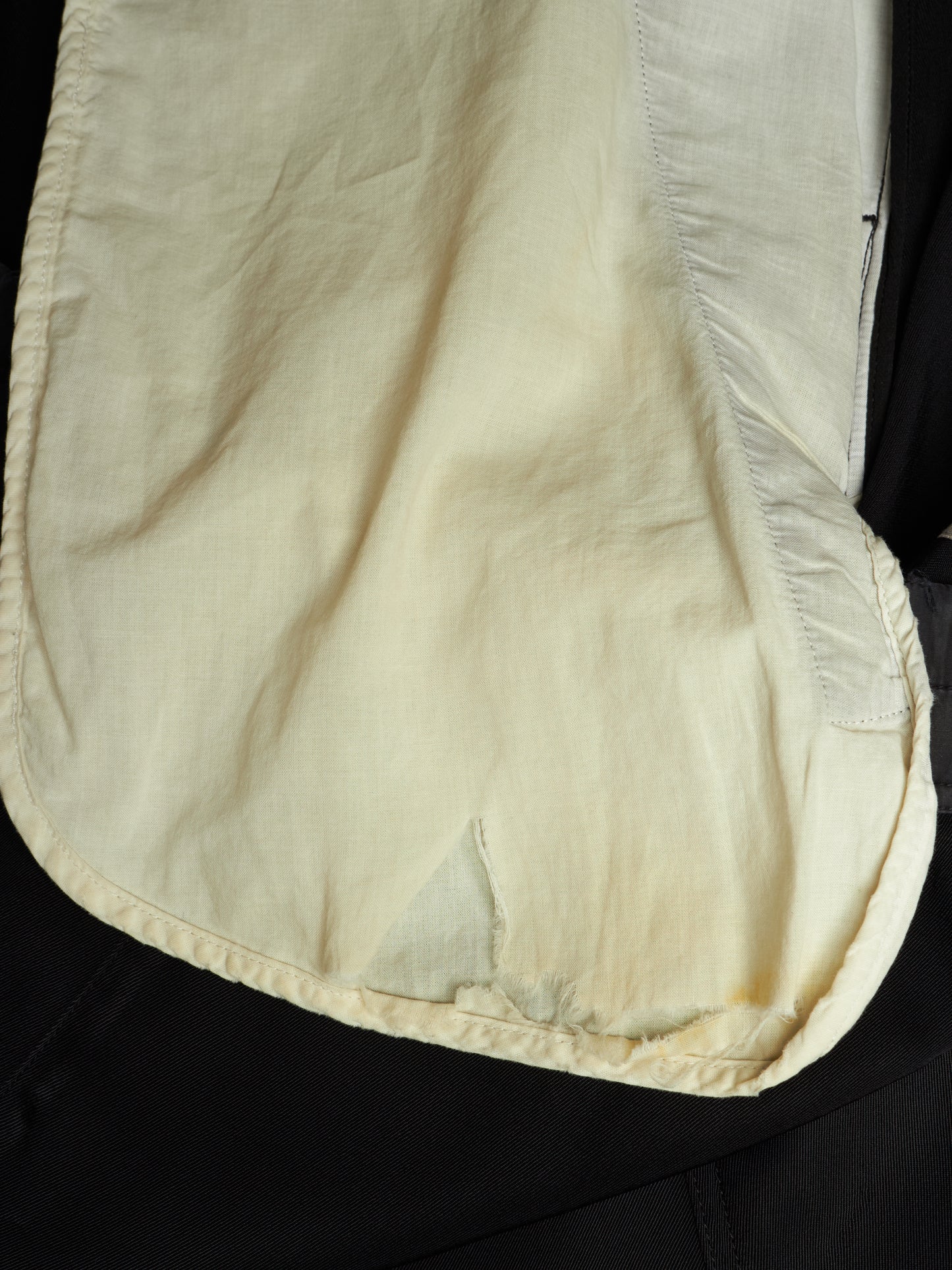A close-up of a cream-colored fabric pouch or cover with visible stitching and a textured woven material, laid against a black background.