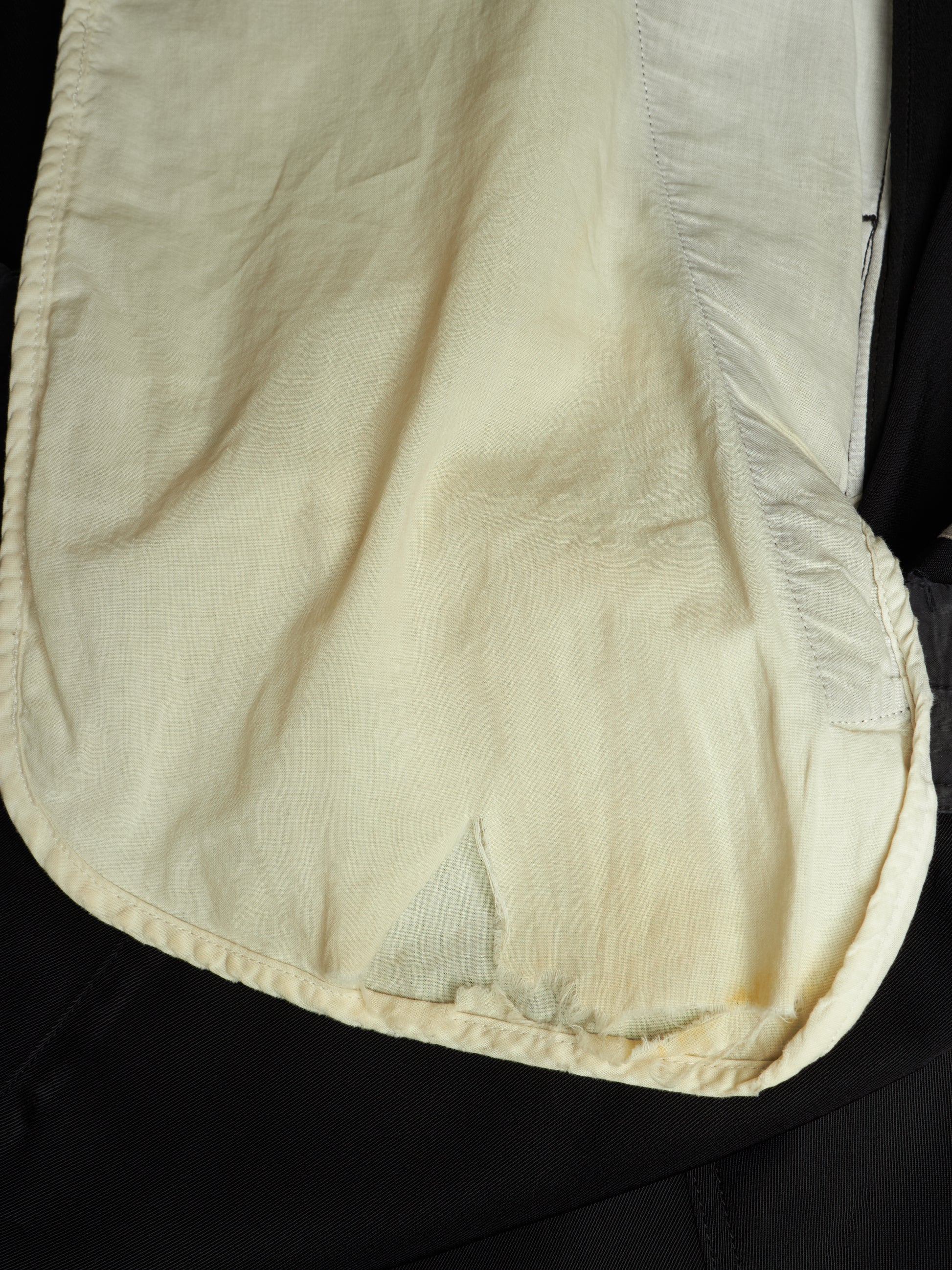 A close-up of a cream-colored fabric pouch or cover with visible stitching and a textured woven material, laid against a black background.