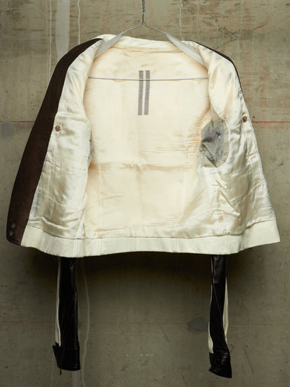 A vintage quilted jacket with a cream satin lining and dark brown sleeves, hanging on a wire hanger against a textured concrete wall.