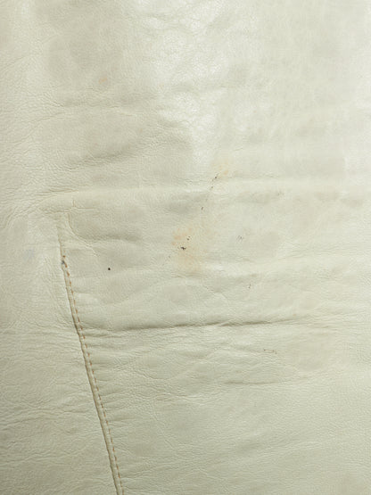 A close-up of a light cream or off-white leather surface with visible grain, stitching, and a small faint stain or discoloration.