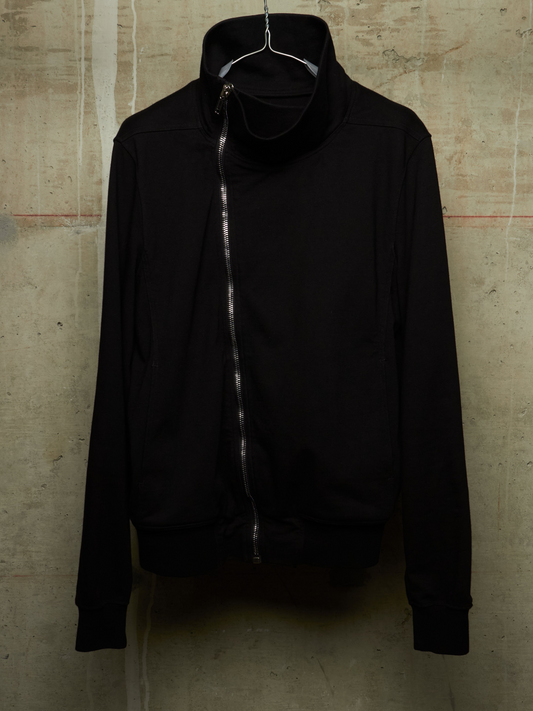 A black zip-up jacket with a high mock neck collar, hanging on a wire hanger against a textured concrete wall.