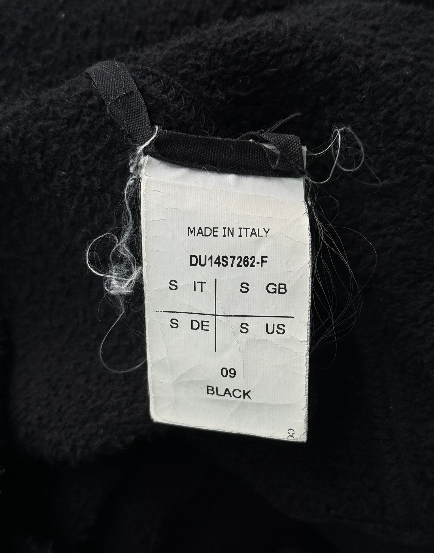 Clothing tag on a black fabric background with 'Made in Italy' text.