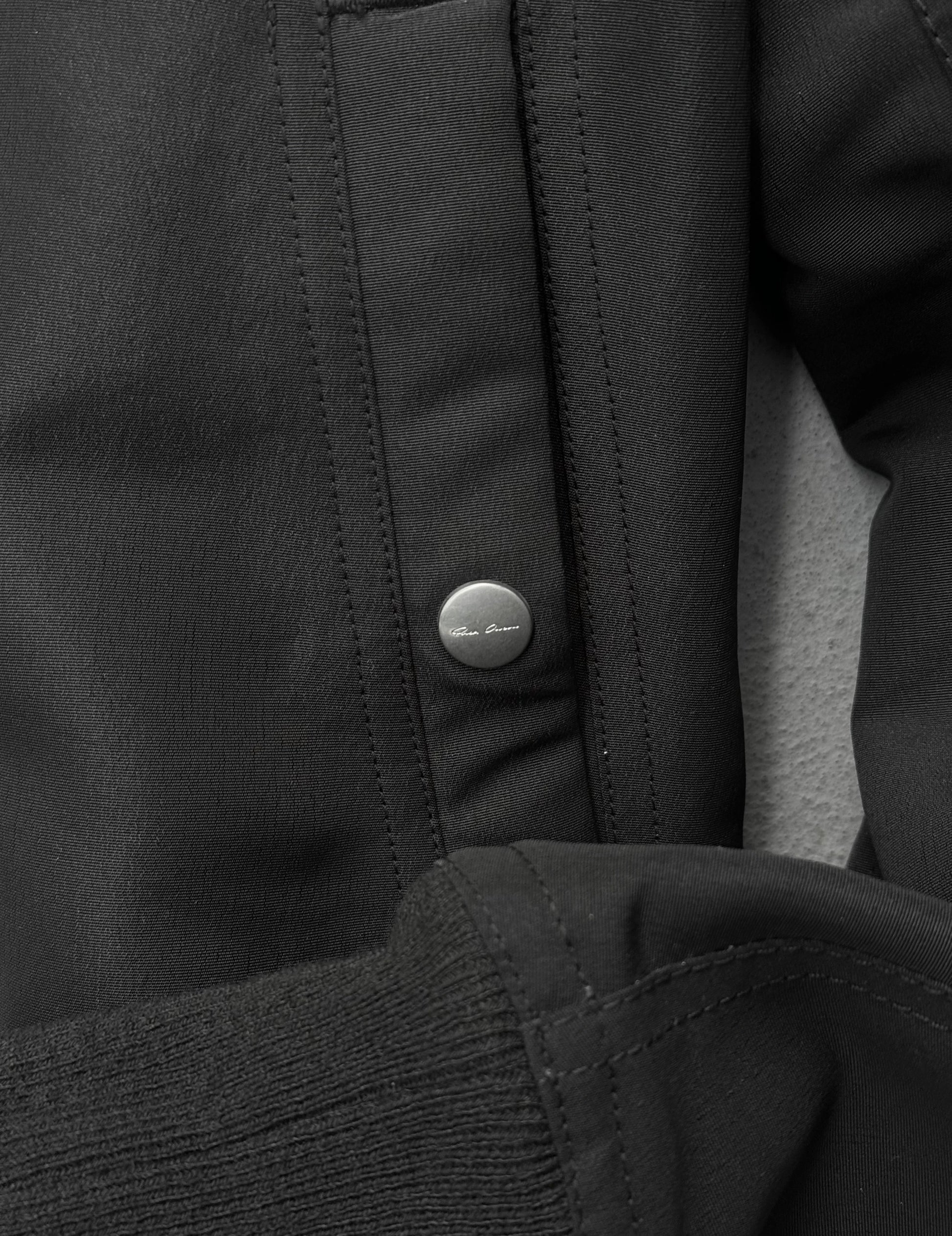 Close-up of a black jacket with a button, featuring the brand logo.