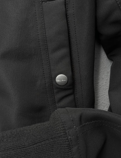 Close-up of a black jacket with a button, featuring the brand logo.