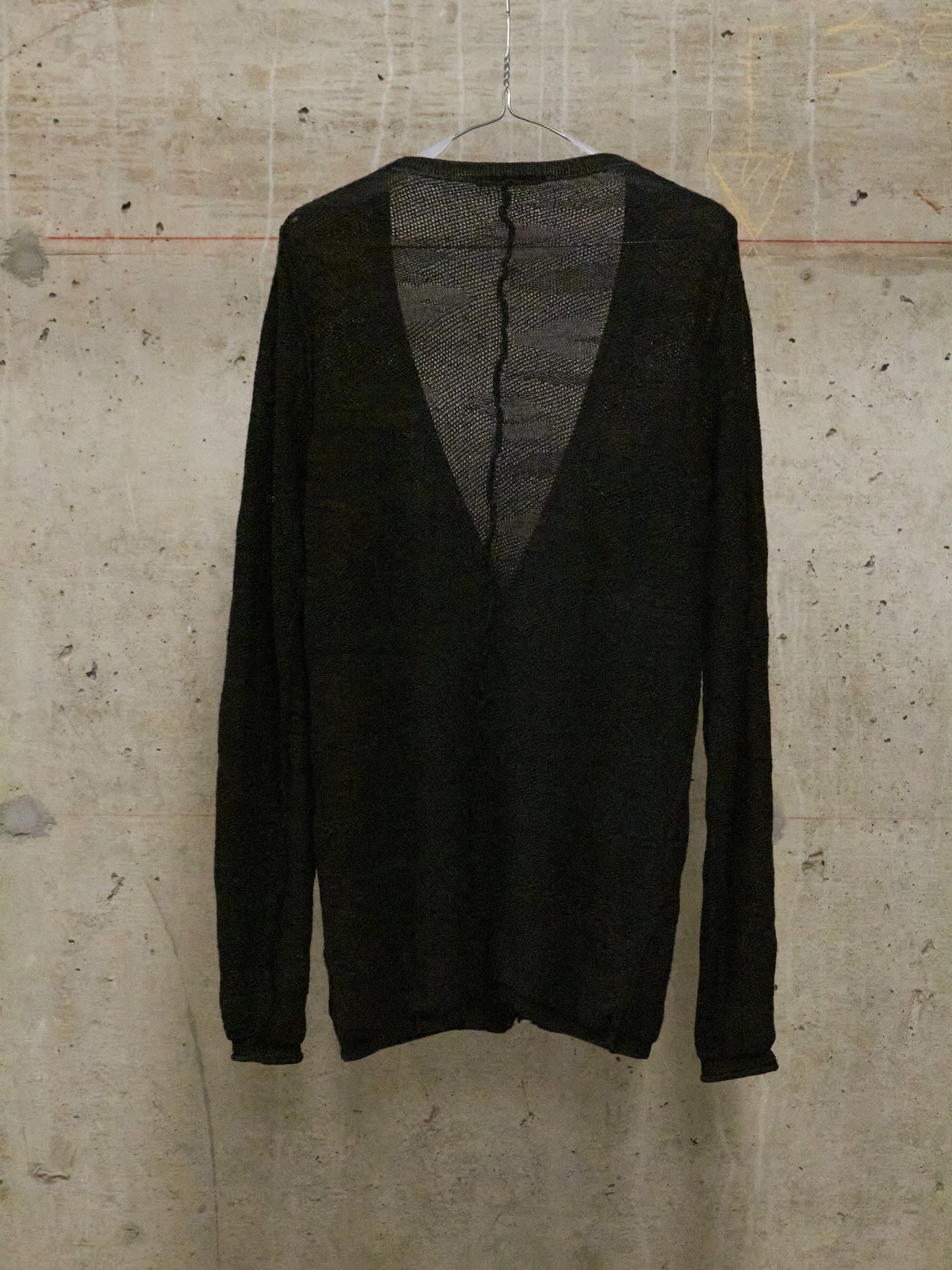 Black sweater on a hanger against a textured beige wall