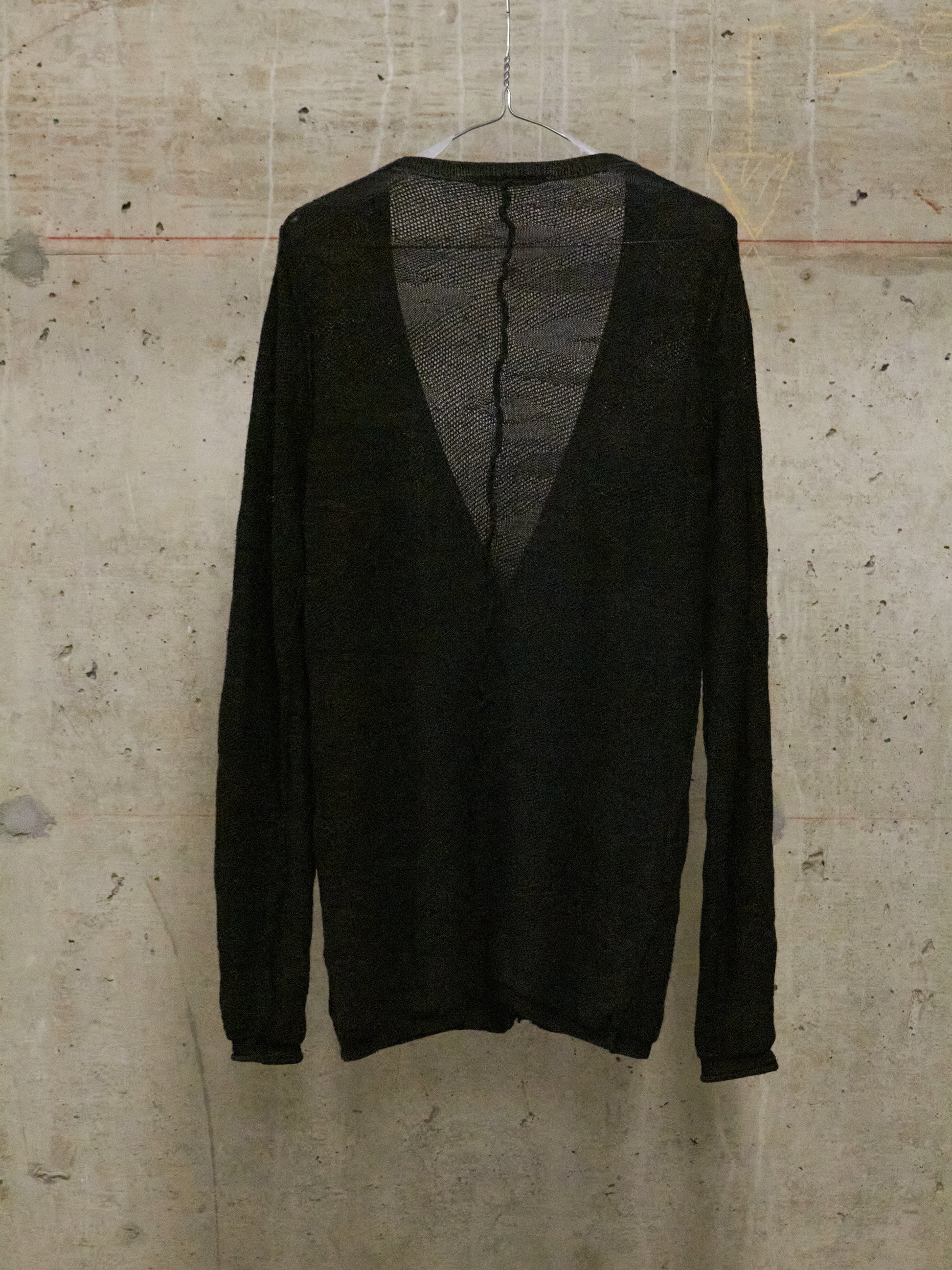Black sweater on a hanger against a textured beige wall