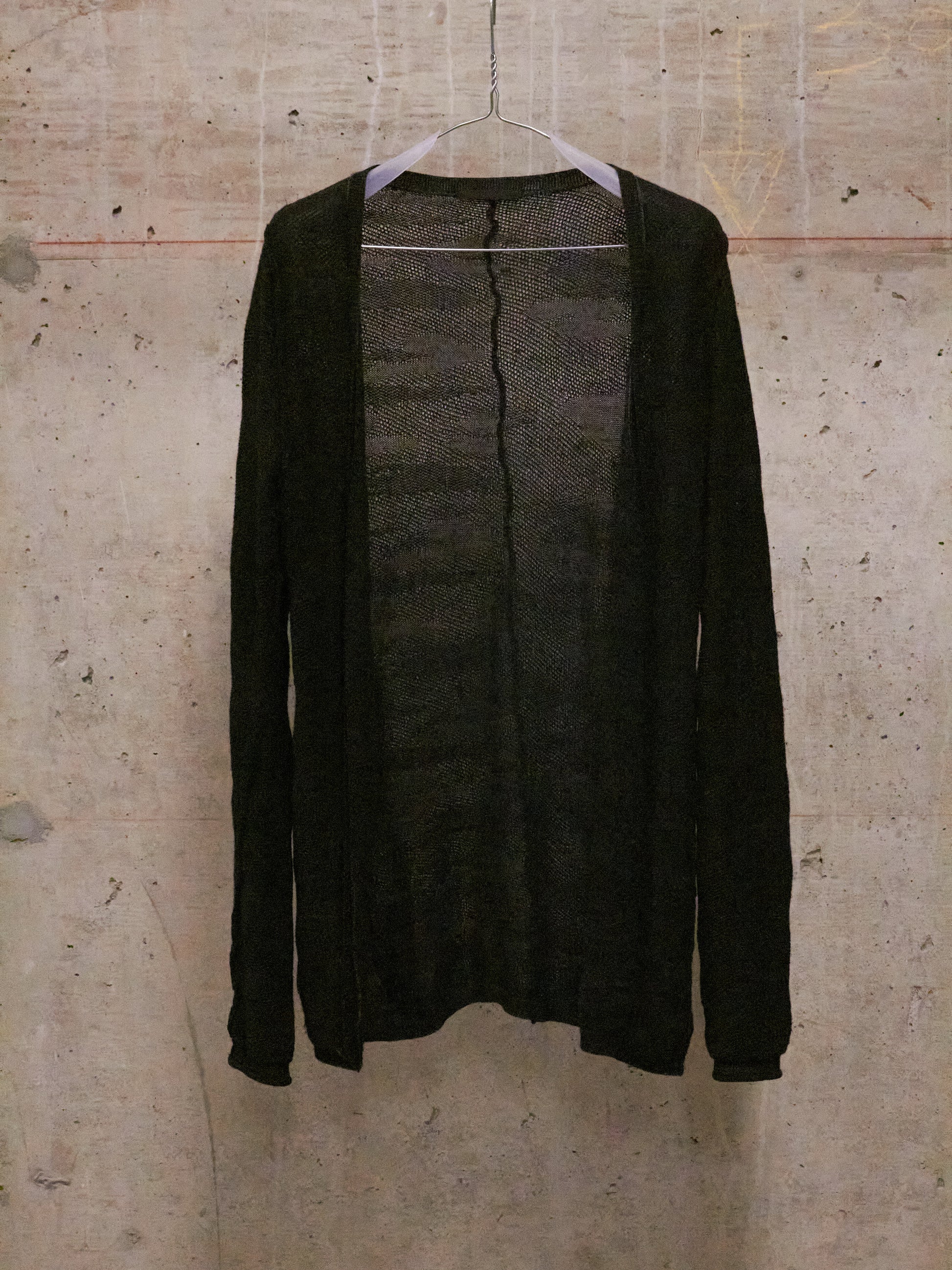 Dark gray cardigan on a hanger against a textured beige wall