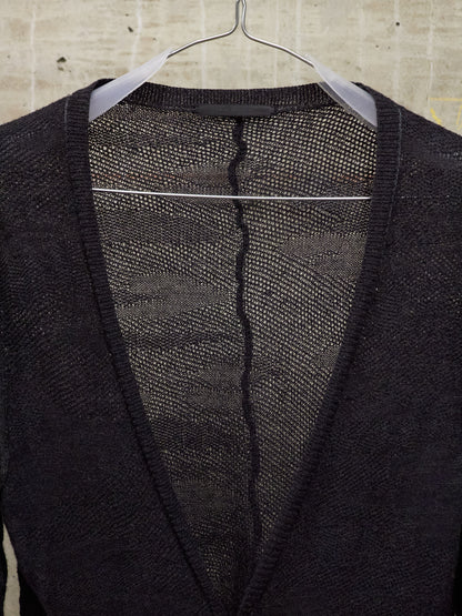 Black cardigan with a visible tear on a hanger against a beige tiled wall.