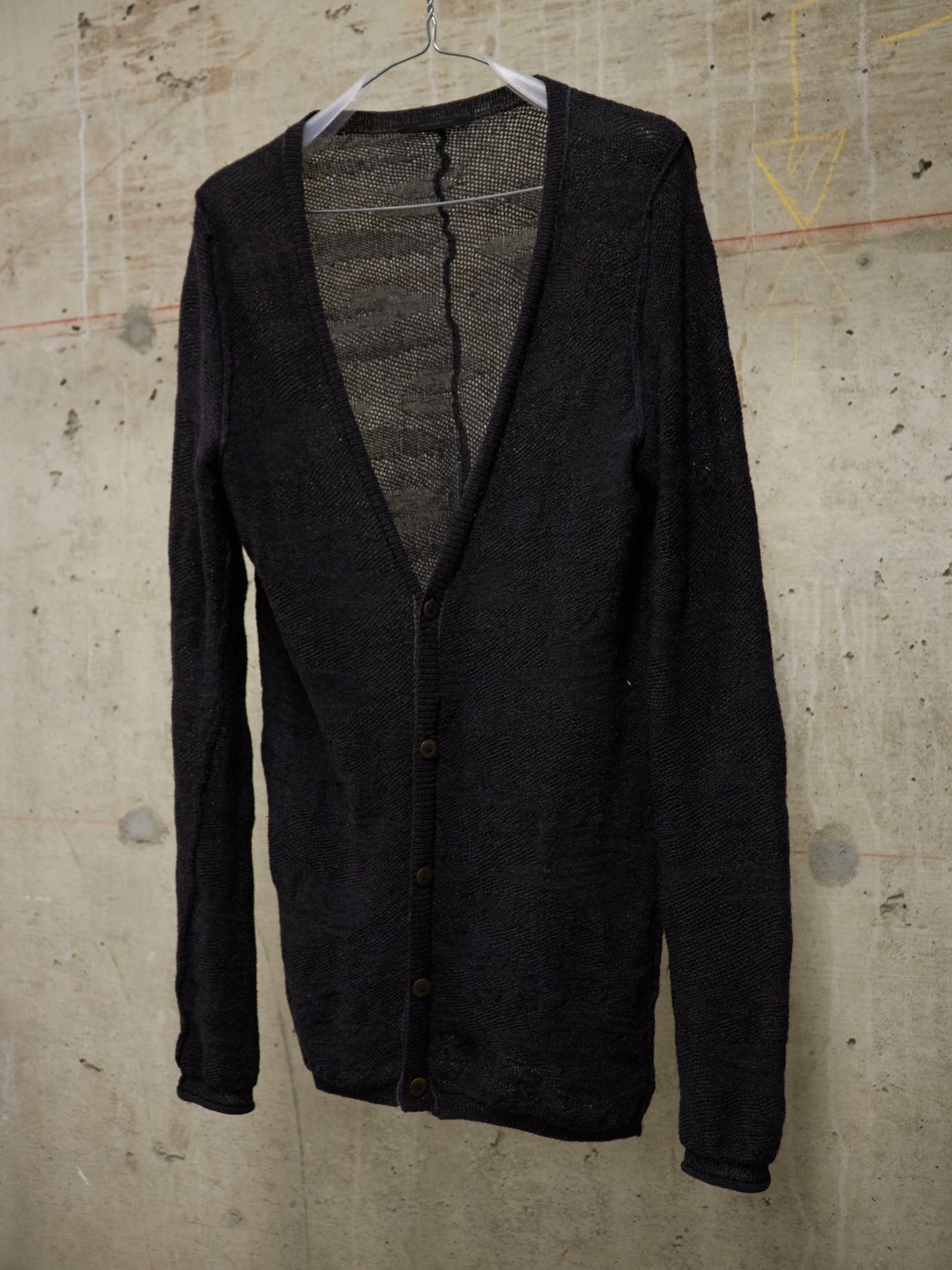 Black cardigan on a hanger against a textured beige wall