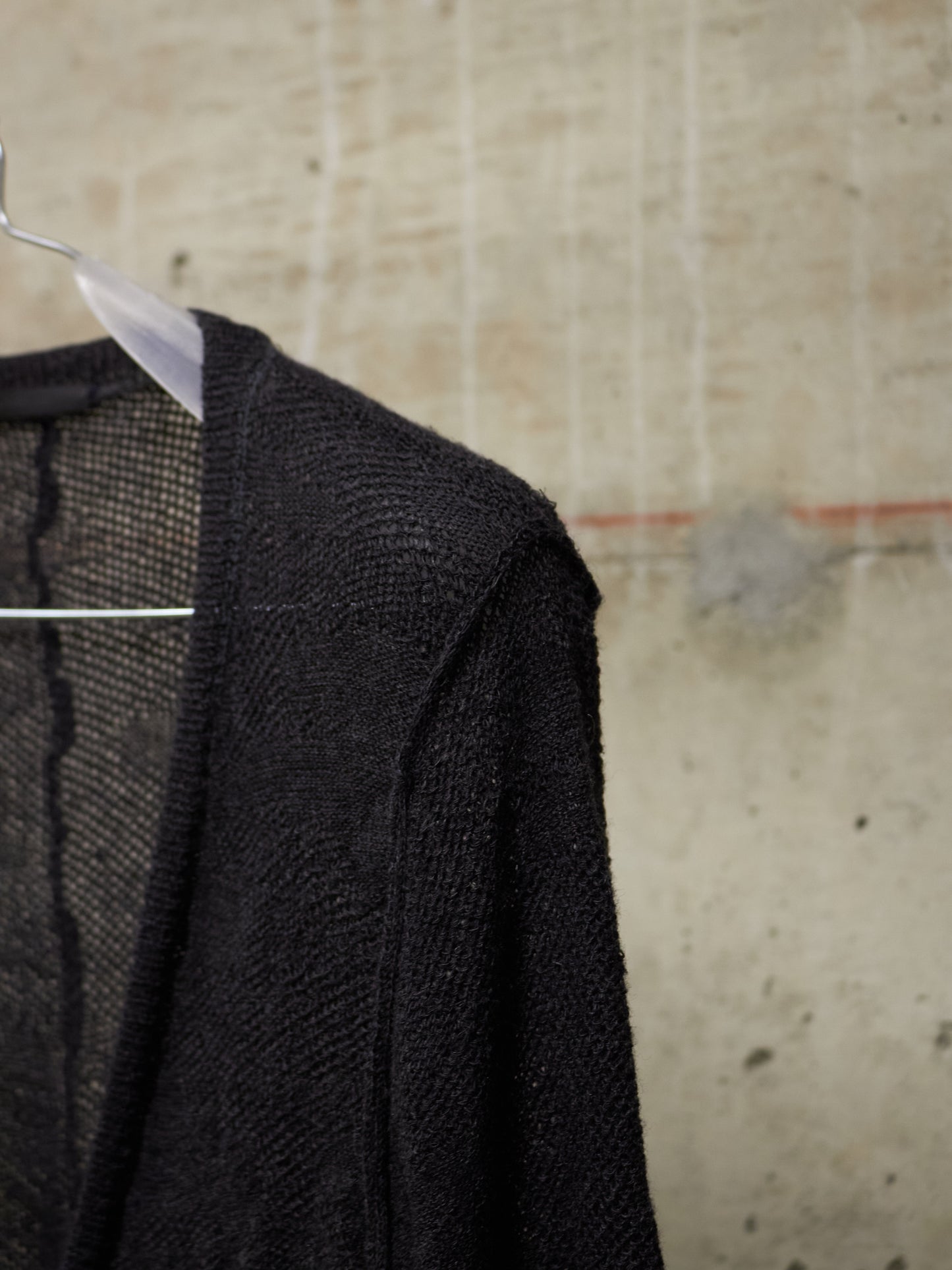 Black textured sweater on a hanger against a textured beige wall.