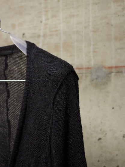 Black textured sweater on a hanger against a textured beige wall.