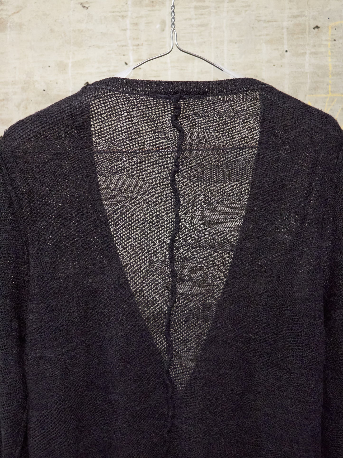 Dark textured jacket on a hanger against a concrete wall.
