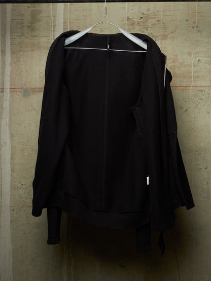 A black zip-up jacket hanging on a white hanger against a textured concrete wall.