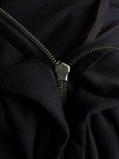 Close-up of a black zippered garment with a dark metal zipper pull and zipper teeth, showing the fabric texture and construction details.