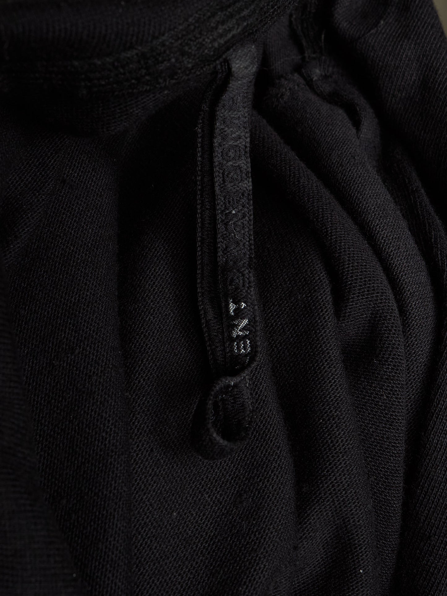 Close-up of a black textured knit garment with a matching black drawstring and a small white debossed brand name reading 'ENT' on the cord.