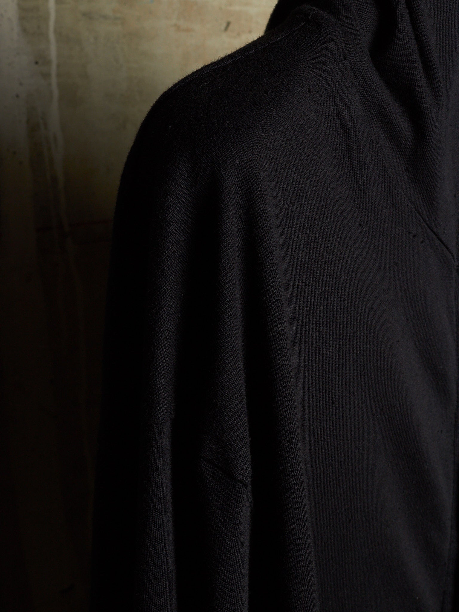 A close-up shot of a black knit garment, likely a sweater or pullover, showing the texture of the fabric against a dark, moody background.