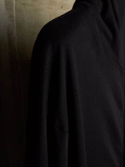 A close-up shot of a black knit garment, likely a sweater or pullover, showing the texture of the fabric against a dark, moody background.