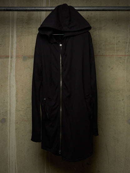 A black hooded jacket with a front zipper, hanging on a metal rack against a textured concrete wall.