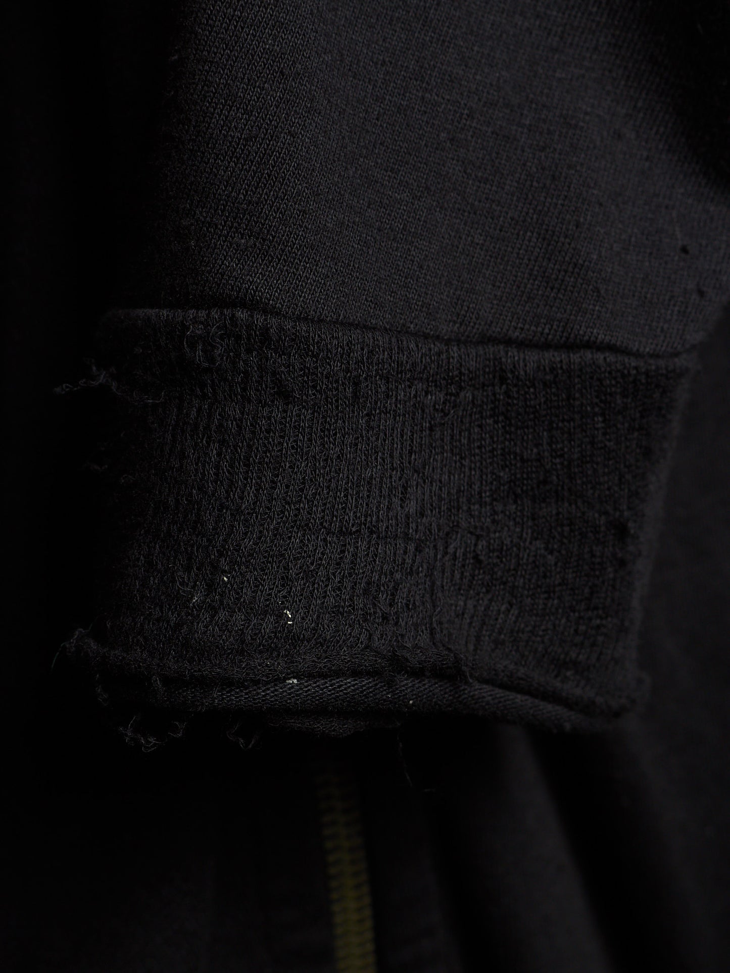 Close-up of a black ribbed knit cuff with frayed, distressed edges on a dark garment.