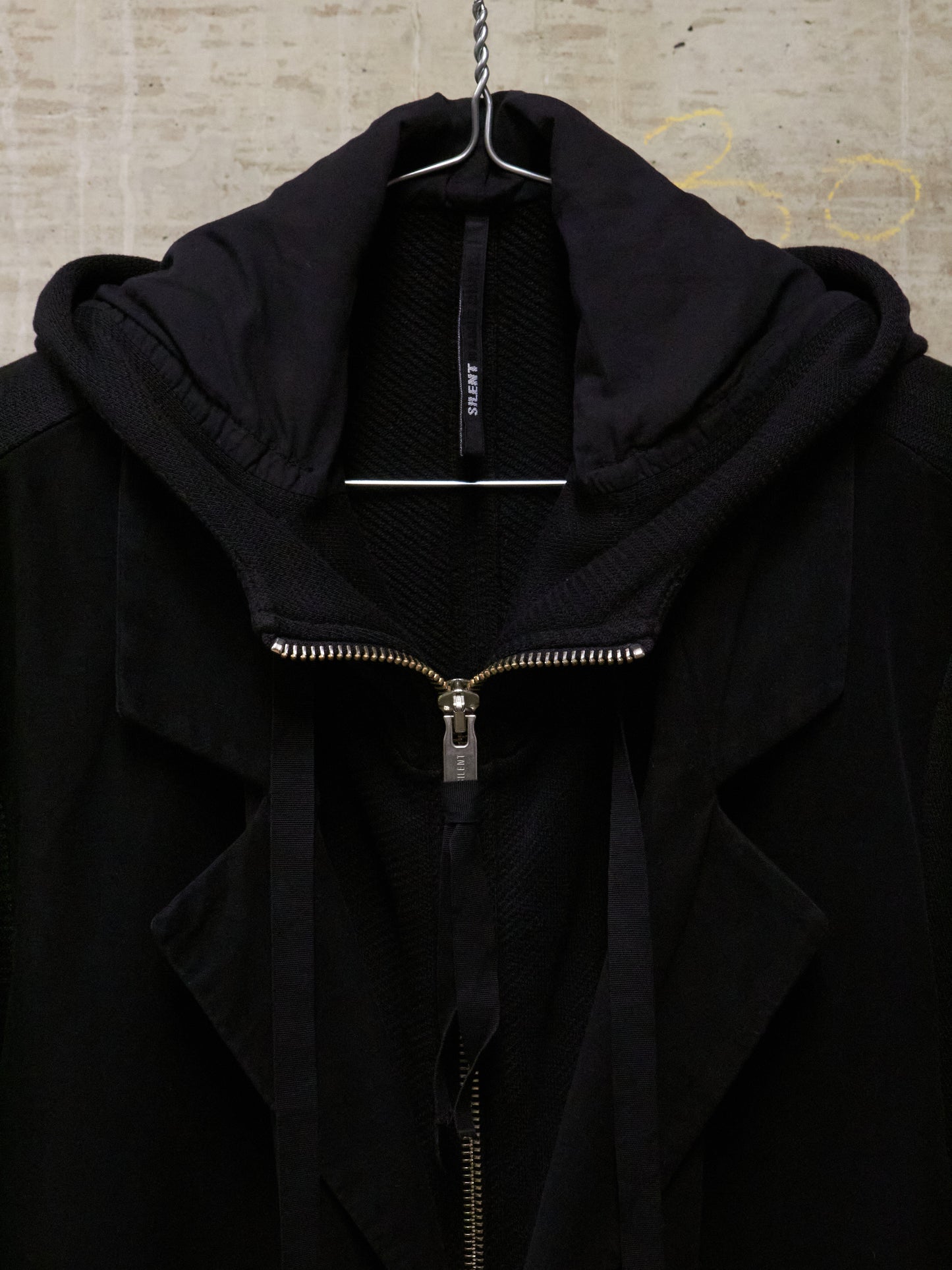 Black jacket with a zipper on a hanger against a textured wall.
