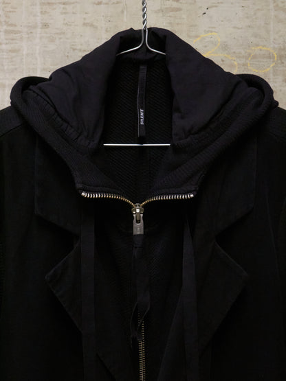 Black jacket with a zipper on a hanger against a textured wall.