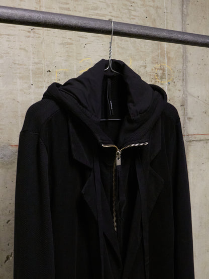 Black jacket with a gold zipper on a hanger against a concrete wall.