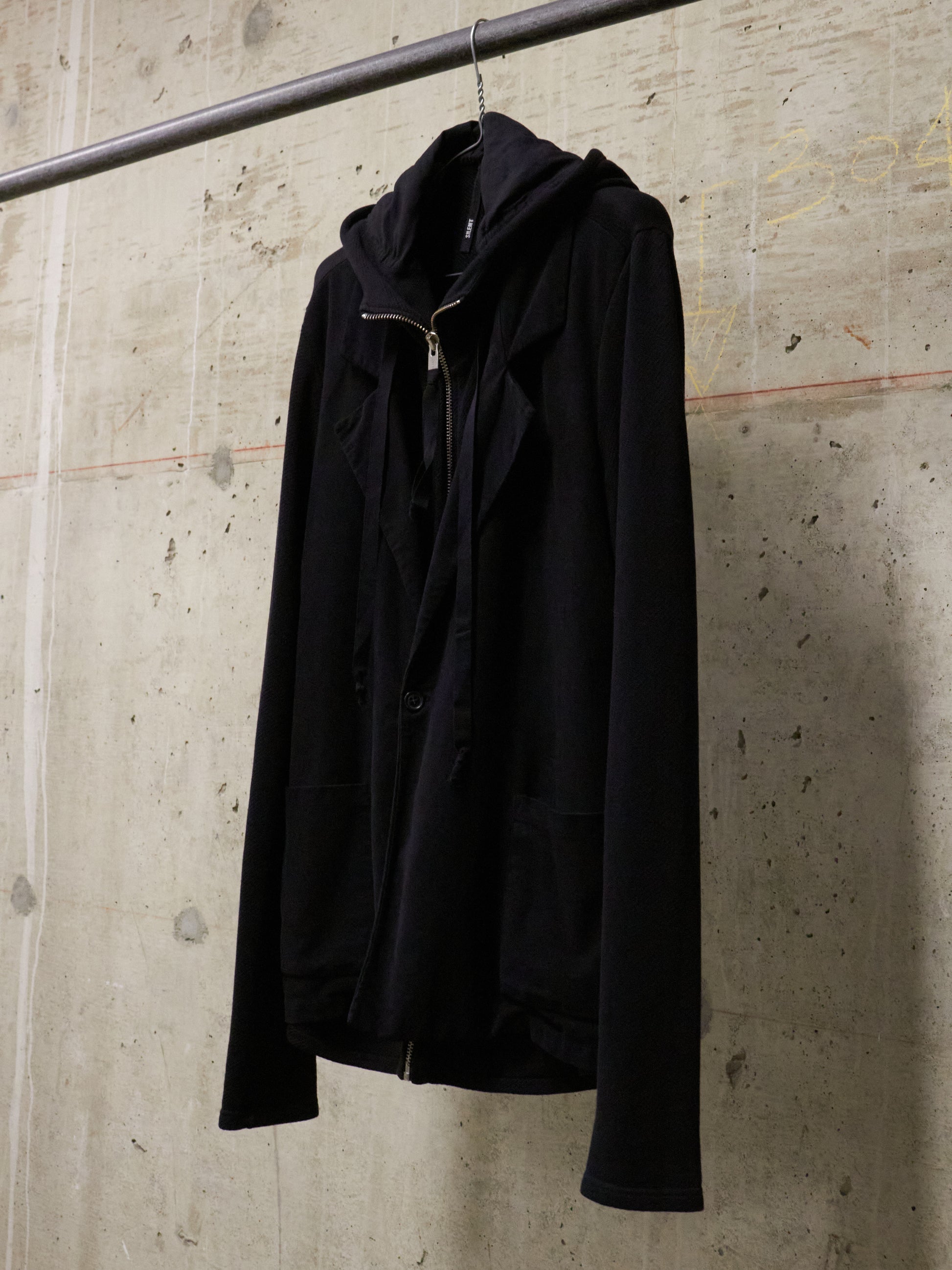 Black jacket hanging on a rack against a textured wall.