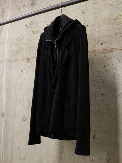 Black jacket hanging on a rack against a textured wall.