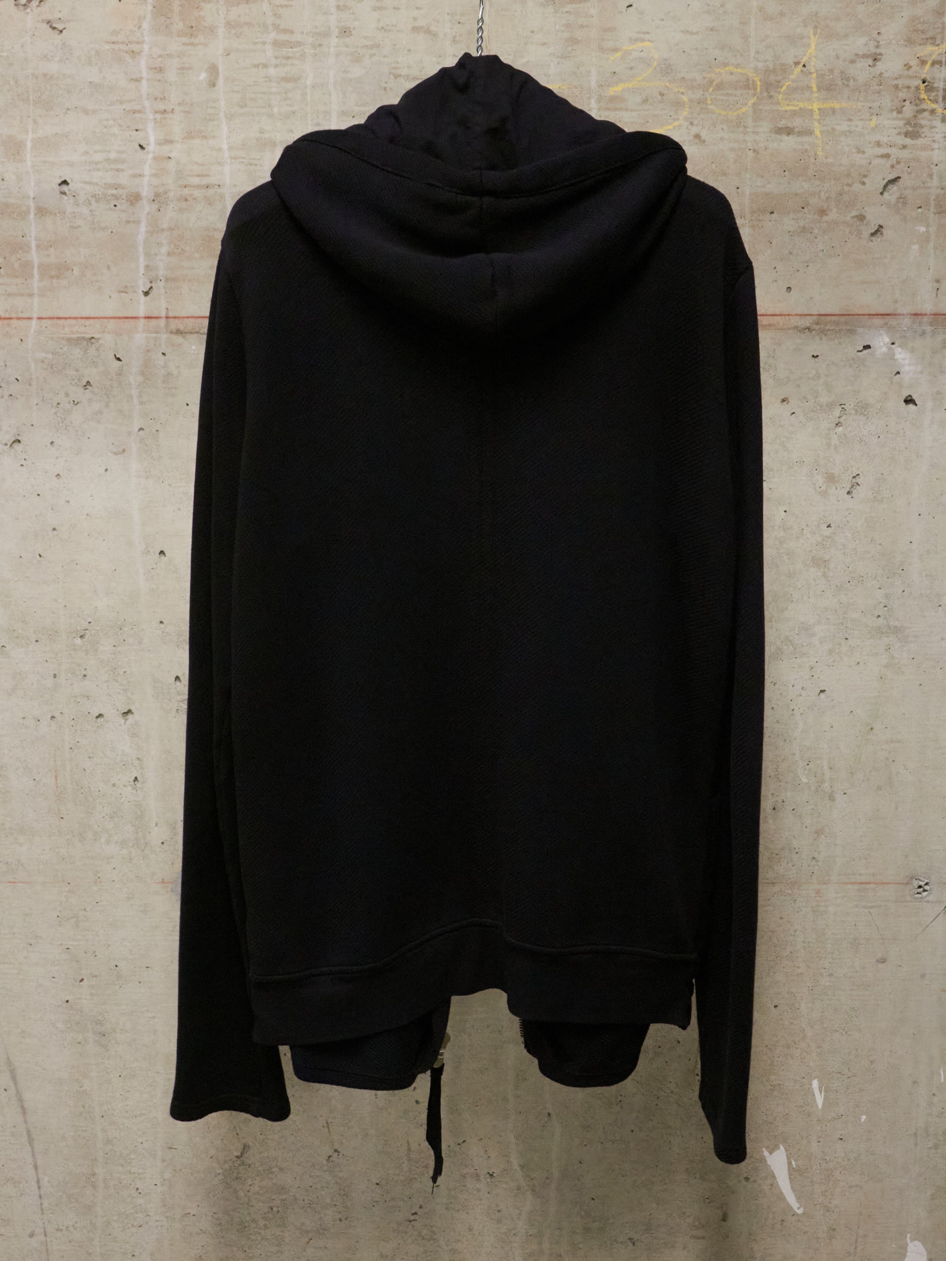 Black hoodie hanging on a textured beige wall